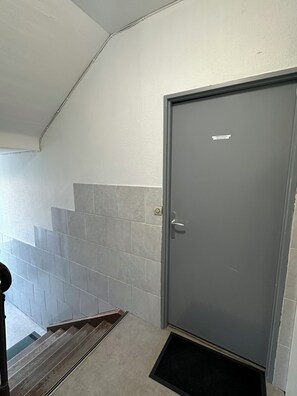 Uma escadaria com ladrilhos cinzentos que leva a uma porta cinzenta com uma placa.