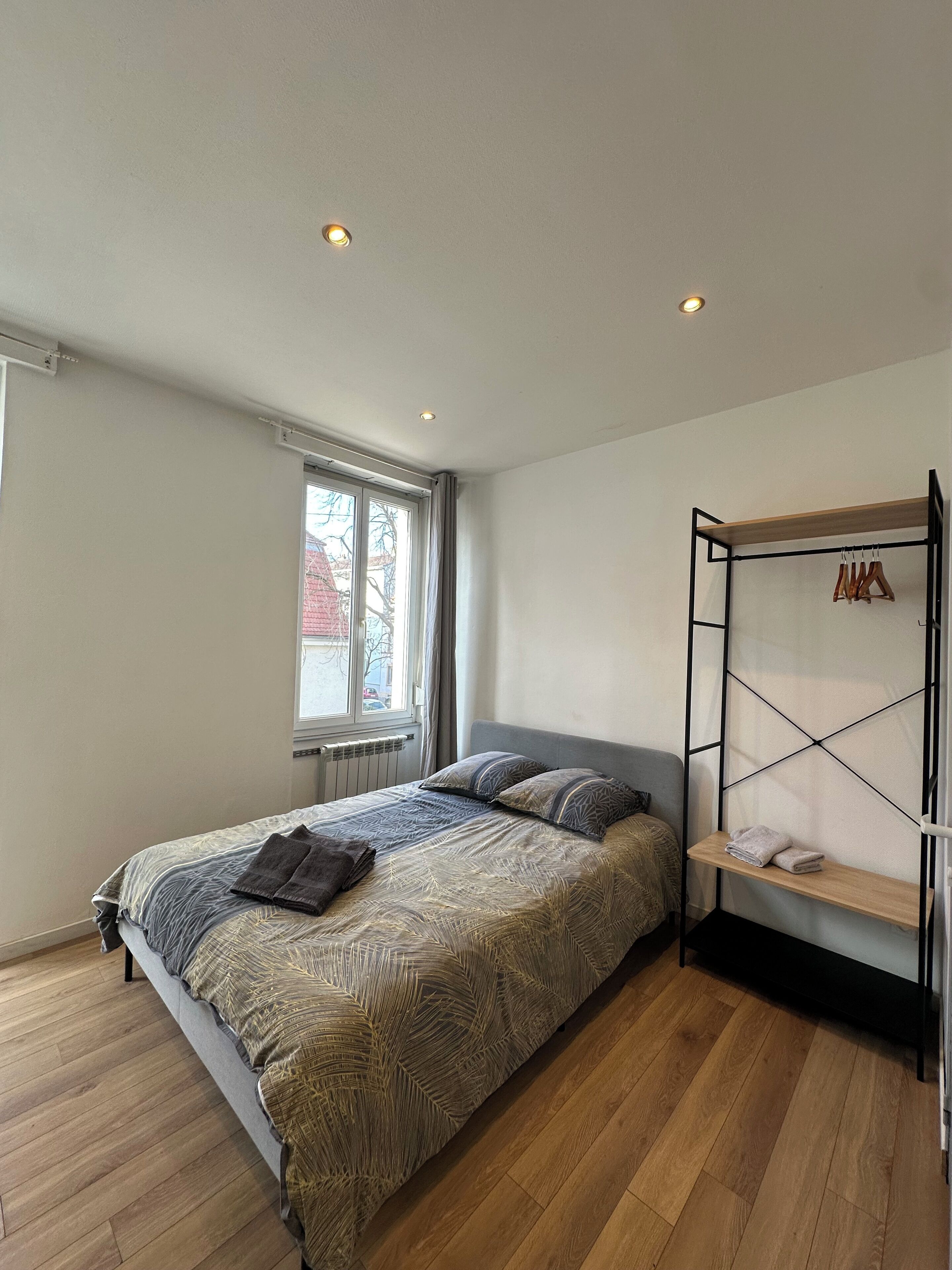 Un dormitorio con cama, ventana, radiador y suelo de madera.