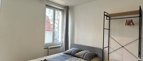 A bedroom with a bed, a window, a radiator, and a wooden floor.