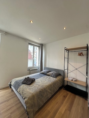 Quarto com cama, janela, radiador e soalho de madeira.