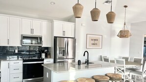 Una cocina moderna con armarios blancos, electrodomésticos de acero inoxidable y una isla central con taburetes.