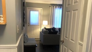 A narrow hallway leading to a living room with a sofa and a lamp. - Dragon Fly Lane, St. Ann's Rest & Relax or Explore in the very private setting . (Baddeck)