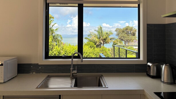 Cuina amb un gran finestral que ofereix una vista panoràmica de l'oceà i vegetació.
