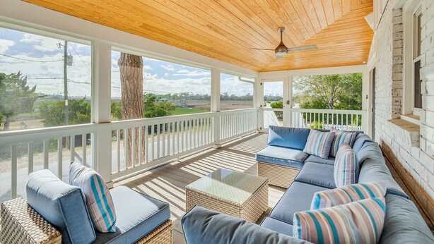 Eine überdachte Veranda mit Holzboden, weißer Geländer und einem großen Ecksofa mit gestreiften Kissen.