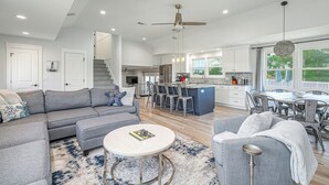 Ein großzügiges Wohnzimmer mit grauem Sofa, einem runden Couchtisch und einem Essbereich mit einer großen Kochinsel und Stühlen.