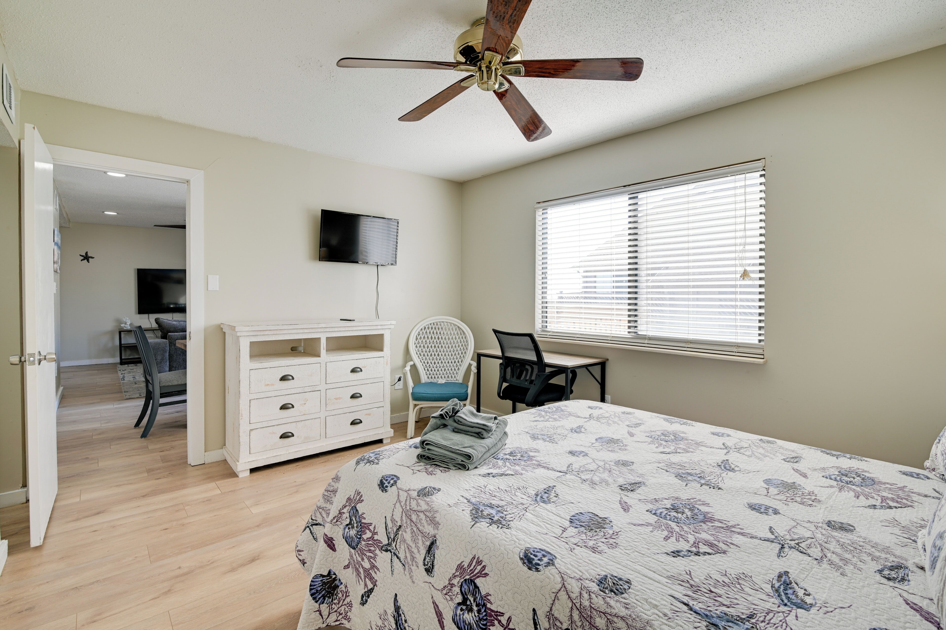 Une chambre à coucher comprenant un lit, un bureau, une chaise, un téléviseur et un ventilateur de plafond.