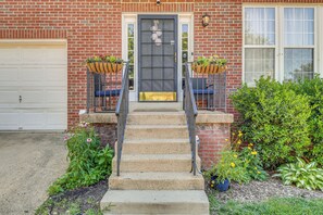 A brick house with a front door, a garage, and a small front yard with steps leading to the door.