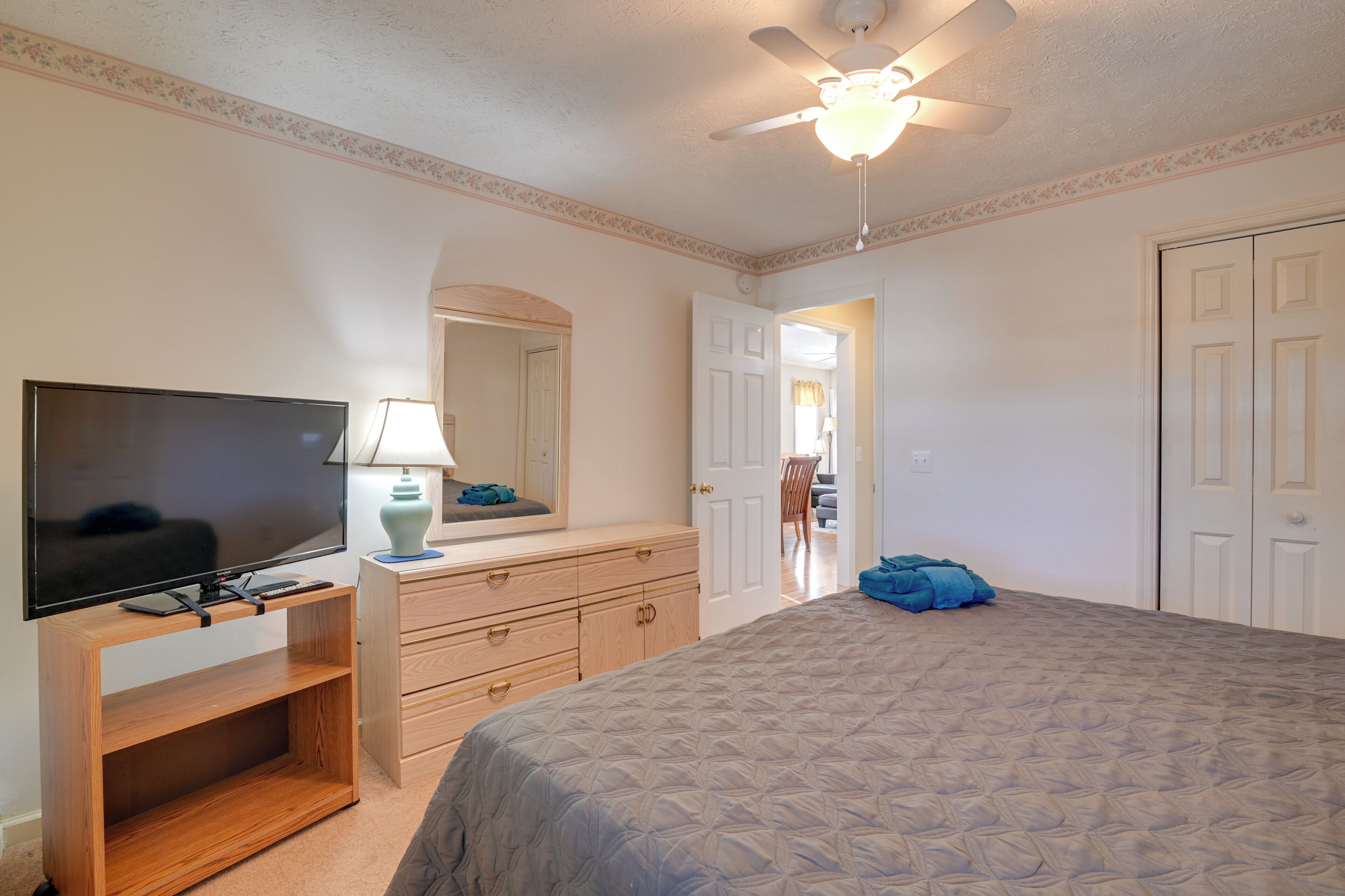 Une chambre à coucher avec un lit, une télévision, une commode et un ventilateur de plafond.