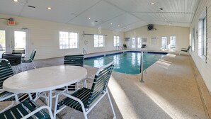 Una piscina al coperto con soffitto bianco, sedie verdi e tavolo bianco.