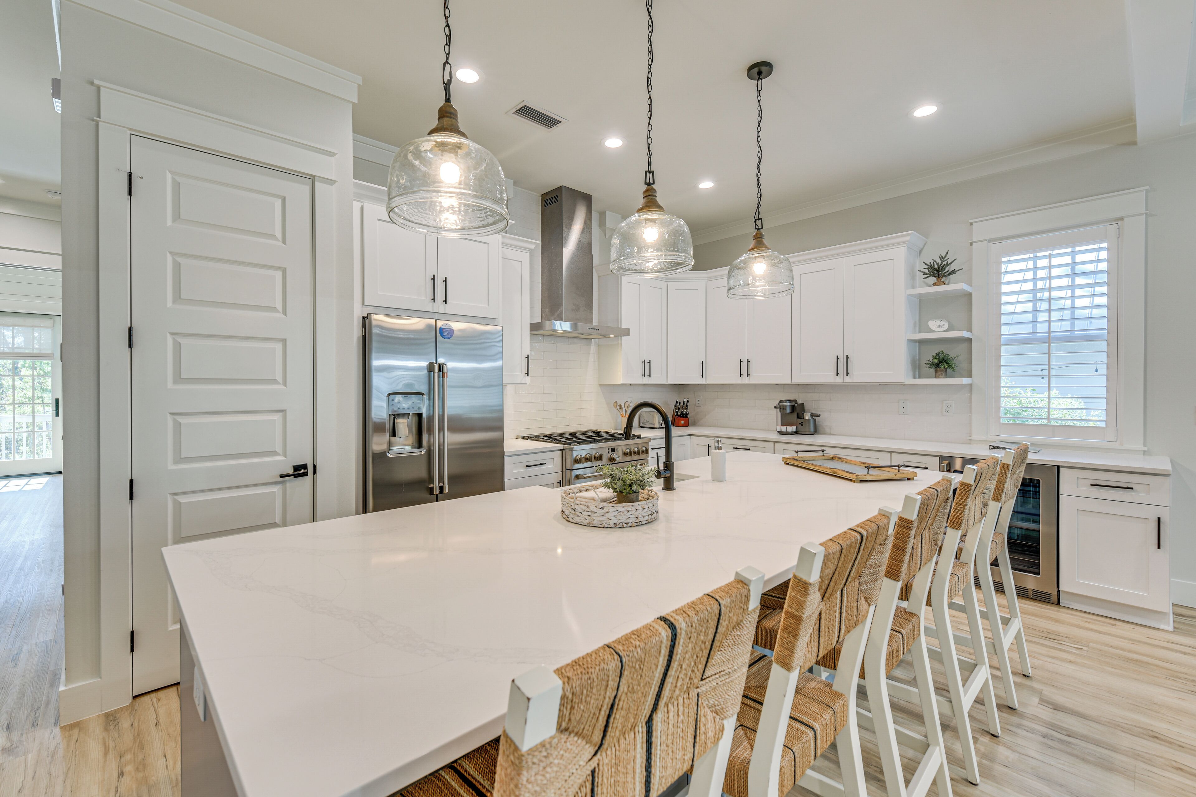 Une cuisine moderne avec des meubles blancs, un grand îlot central et des luminaires suspendus.