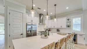 A modern kitchen with white cabinetry, a large island, and hanging pendant lights. - Walk to Gulf: Modern Retreat in Santa Rosa Beach! (Santa Rosa Beach)