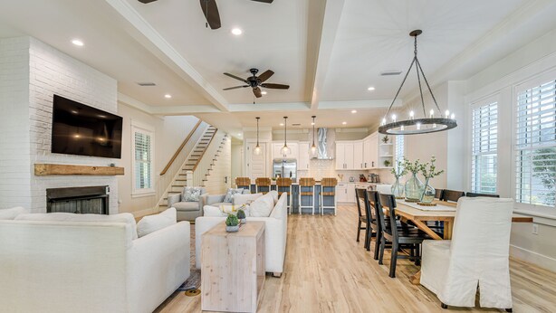 A spacious living area with a fireplace, white sofas, a wooden coffee table, and a dining area with a chandelier. - Walk to Gulf: Modern Retreat in Santa Rosa Beach! (Santa Rosa Beach)