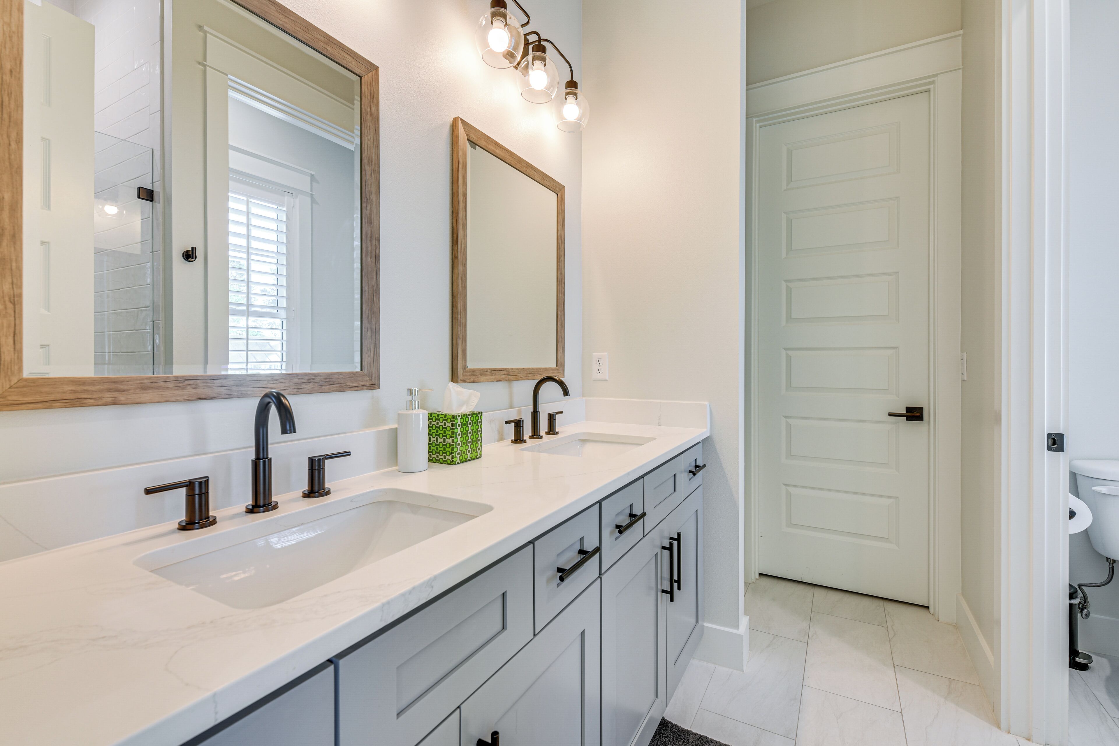 A bathroom with two sinks, a large mirror, and a door leading to another room.
