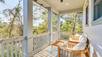 Une véranda couverte avec un ventilateur de plafond, des meubles en bois et une vue sur les arbres et le ciel.