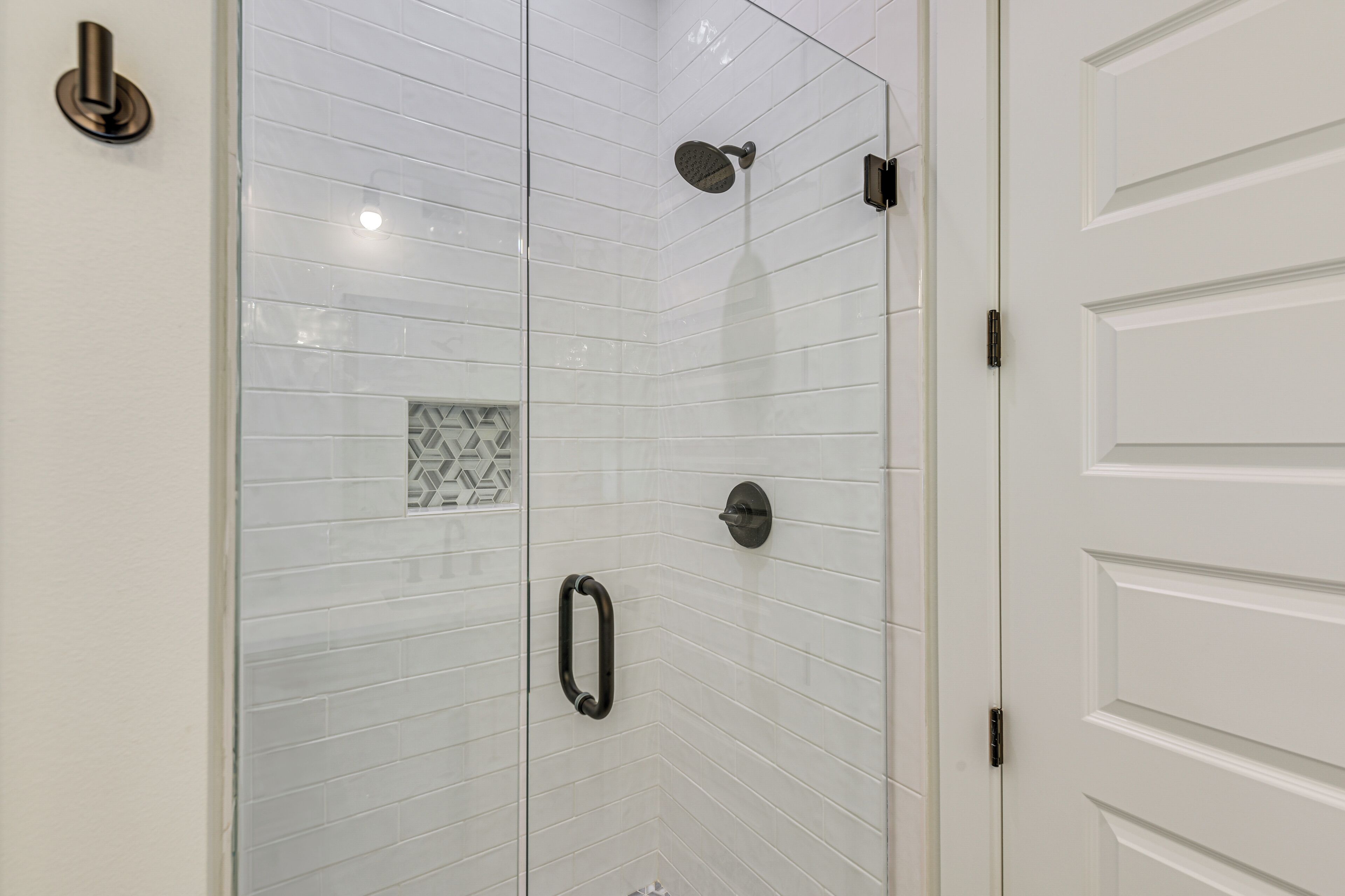 A glass-enclosed shower with white tiles and a geometric pattern tile.
