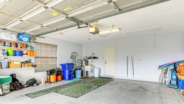 Een garage met een betonnen vloer, planken met verschillende spullen, een werkbank en een deur.