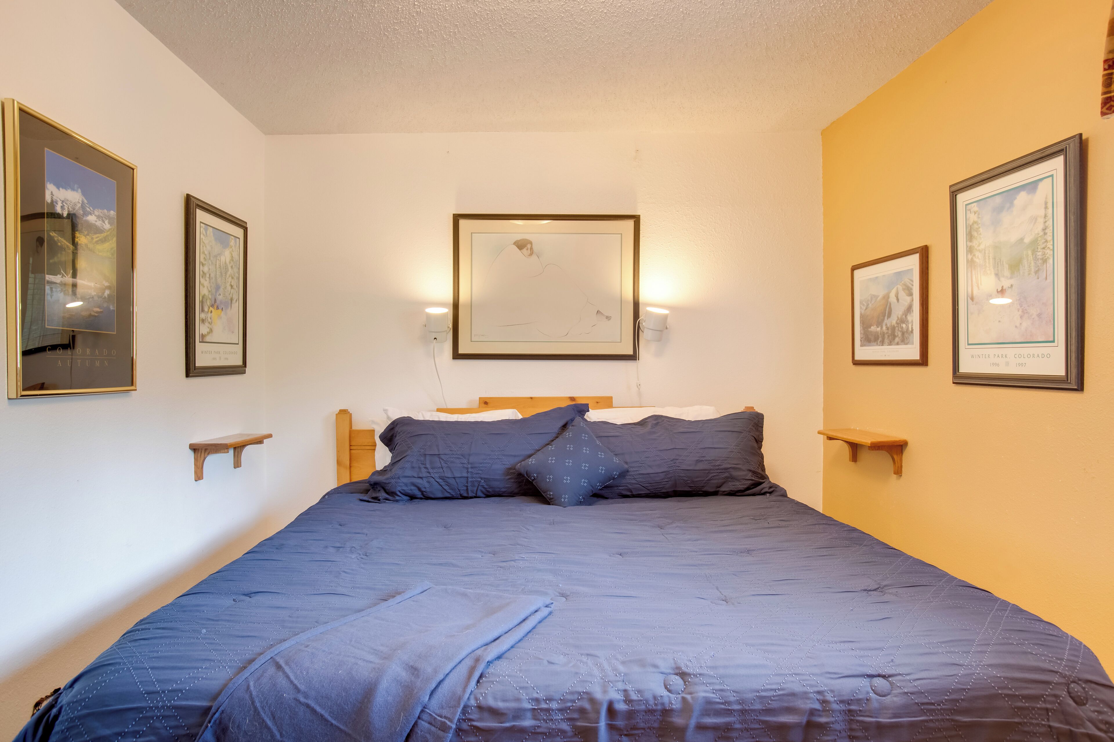 Une chambre avec un grand lit, deux tables de chevet et des tableaux encadrés accrochés aux murs.