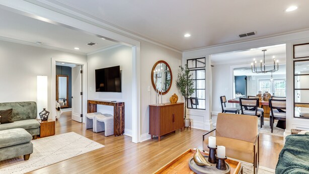 A spacious living room with hardwood floors, a green sofa, a wooden coffee table, and a dining area with a chandelier.