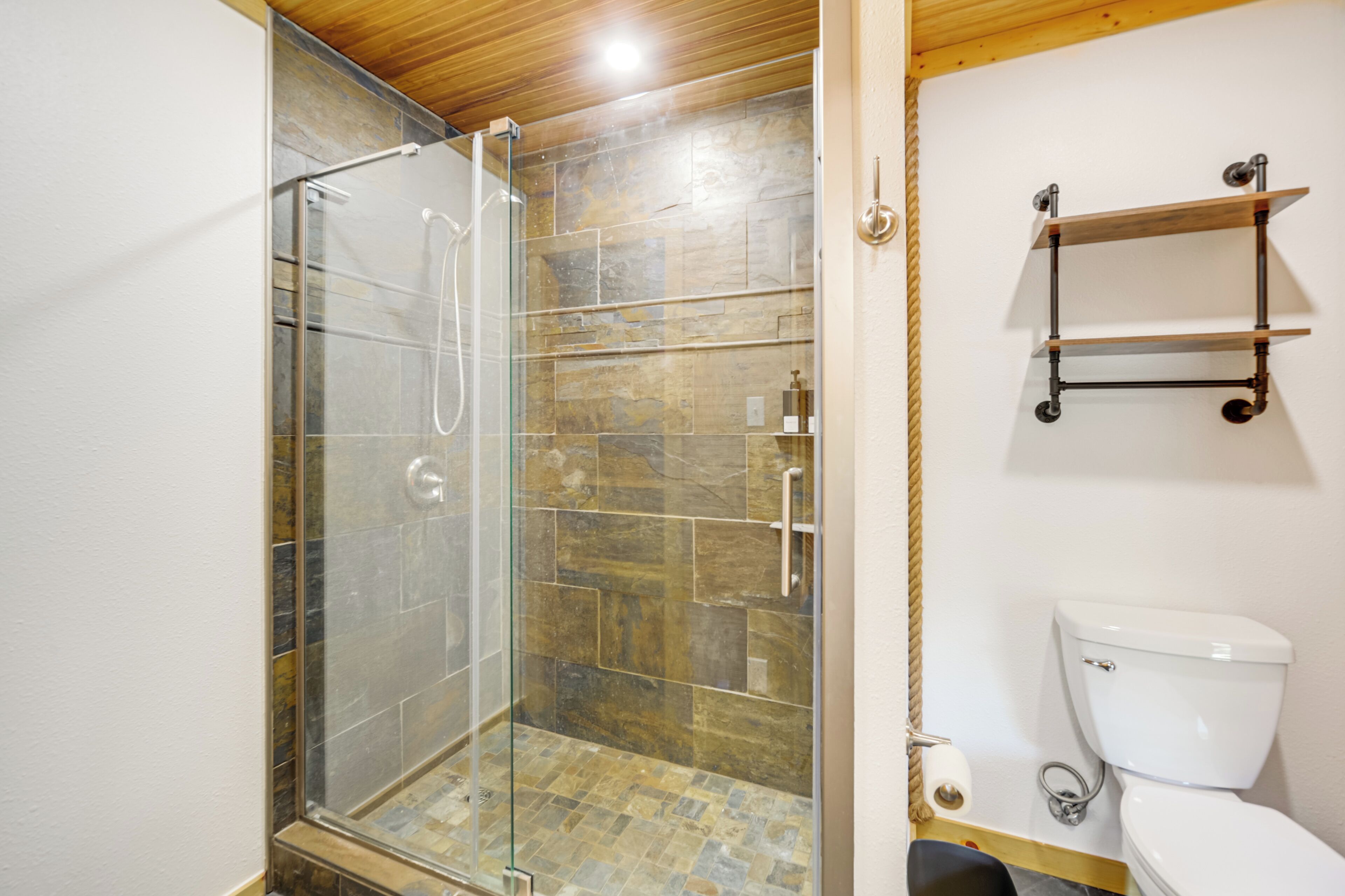 Une salle de bain avec une douche à parois de verre, des toilettes et une étagère contenant des articles de toilette.