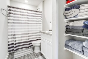 A bathroom with a striped shower curtain, a toilet, and a shelf with folded towels. - 13 Mi to Baton Rouge: Family-friendly Home (Zachary)
