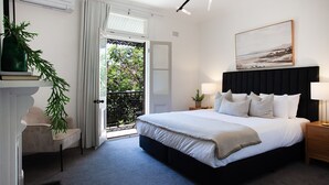 A bedroom with a large bed, bedside lamps, a painting, and a view through the door.