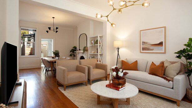 A living room with a sofa, armchairs, a coffee table, and a TV. There is a fireplace, a bookshelf, and a painting on the wall.