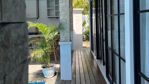 A covered outdoor area with a wooden deck, a stone pillar, a potted plant, and a view of a swimming pool. - Villa Casa Petite 2 (Bali)