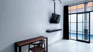 A modern room with a wooden bench, a flat-screen TV mounted on the wall, and a large window offering a view of the sea. - Villa Casa Petite 2 (Bali)