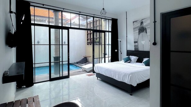 A modern bedroom with a bed, a desk, and a view of an outdoor swimming pool. - Villa Casa Petite 2 (Bali)