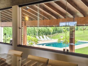 Un interior moderno con un amplio ventanal que da a una piscina y jardín.