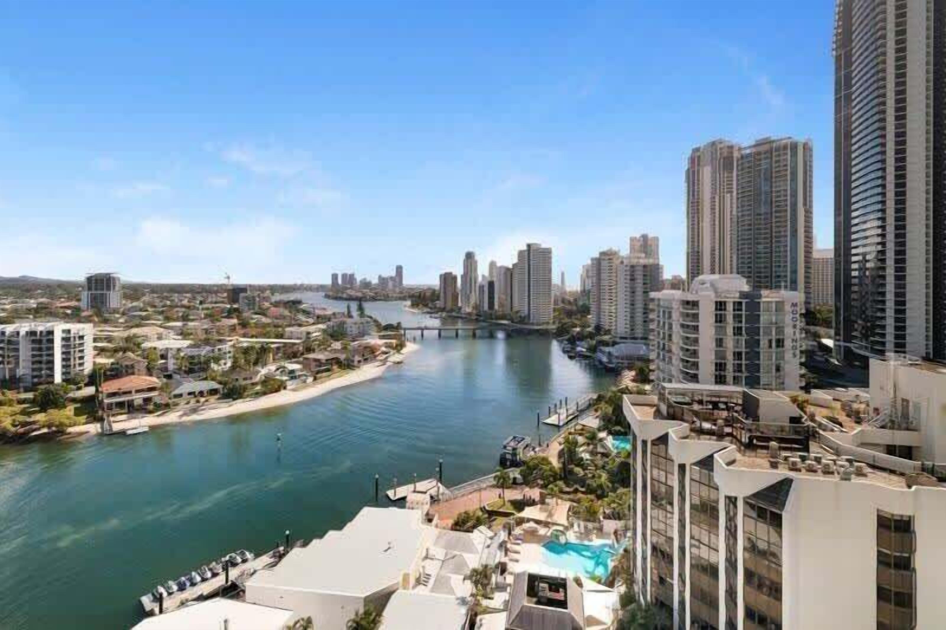 A coastal cityscape with high-rise buildings, a river, and a bridge.