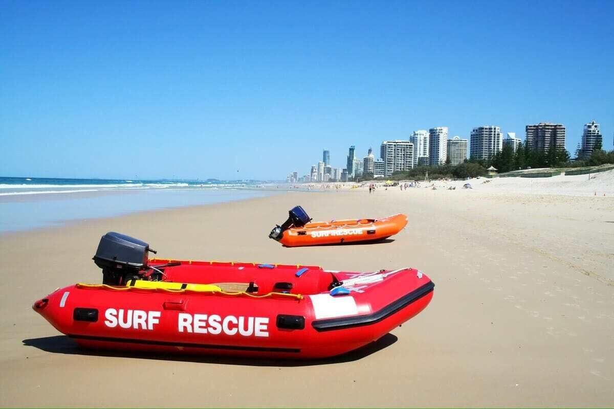 Deux embarcations rouges utilisées pour les opérations de sauvetage en mer, sur une plage de sable, avec une vue sur les gratte-ciel d’une ville en arrière-plan.