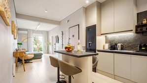 A modern kitchen with a marble countertop, two bar stools, and a dining area with a table and chairs. - Acropolis Path - Elegant Apartment near Plaka (Athina)