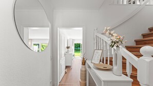 A hallway with a white staircase, a round mirror, and a vase with flowers on a console table.
