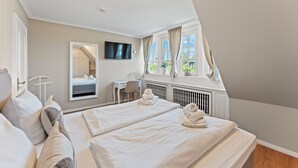 A hotel room with two beds, a desk, a TV, and a window with curtains.