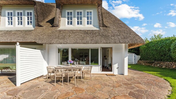 A house with a stone patio, white exterior, and a thatched roof.