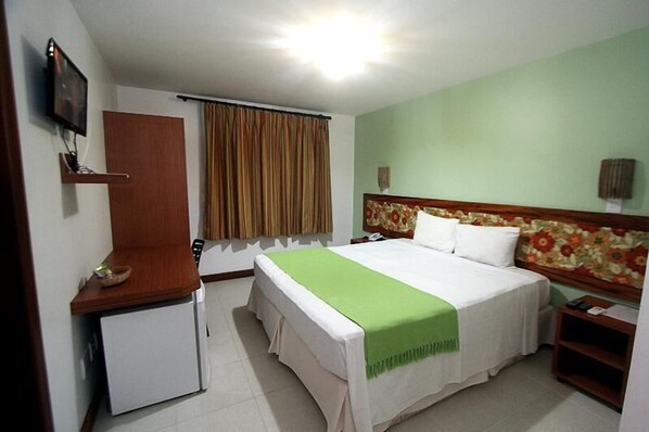 A hotel room with a bed, a small desk, a television, and a window with curtains.