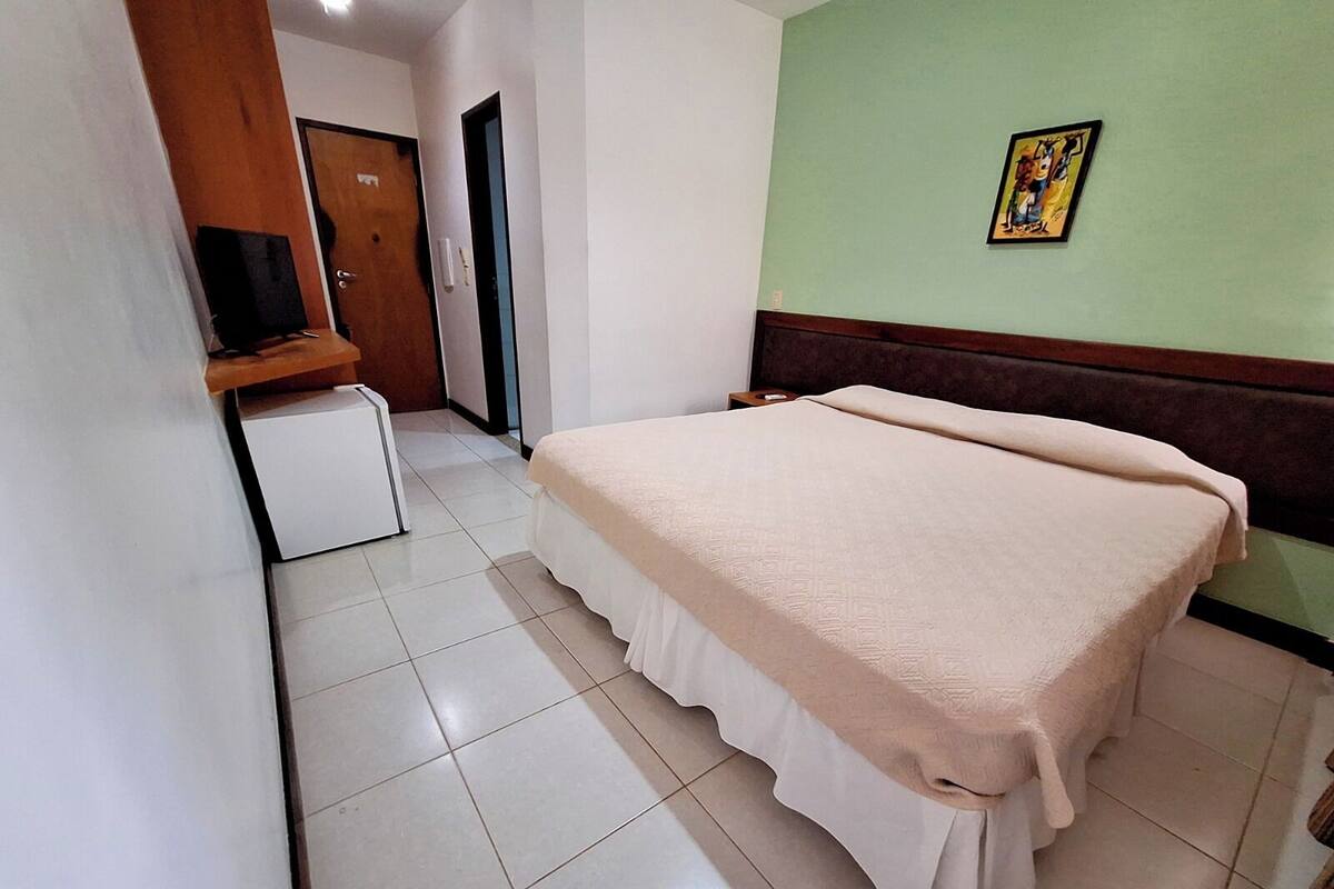 Ein Hotelzimmer mit einem Bett, einem kleinen Kühlschrank, einem Holztisch und einer Tür zu einem anderen Raum.