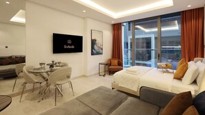 A modern hotel room with a bed, sofa, dining table, and TV. - Modern Studio Near Dubai Mall, Walk to Dubai Canal (Dubai)