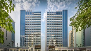 A modern high-rise building with a glass facade, multiple floors, and a central courtyard with palm trees. - Modern Studio Near Dubai Mall, Walk to Dubai Canal (Dubai)