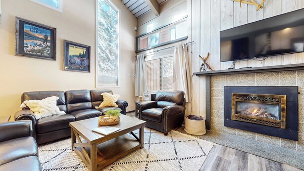 A living room with a fireplace, leather sofas, a coffee table, and framed posters on the wall. - Modern Cabin for 8, Near Slopes + Canyon Lodge! (Mammoth Lakes)