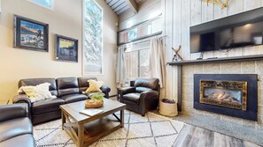 A living room with a fireplace, leather sofas, a coffee table, and framed posters on the wall. - Modern Cabin for 8, Near Slopes + Canyon Lodge! (Mammoth Lakes)