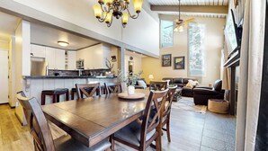 A spacious kitchen with a dining area, a living room with a sofa and a fireplace, and large windows allowing natural light. - Modern Cabin for 8, Near Slopes + Canyon Lodge! (Mammoth Lakes)