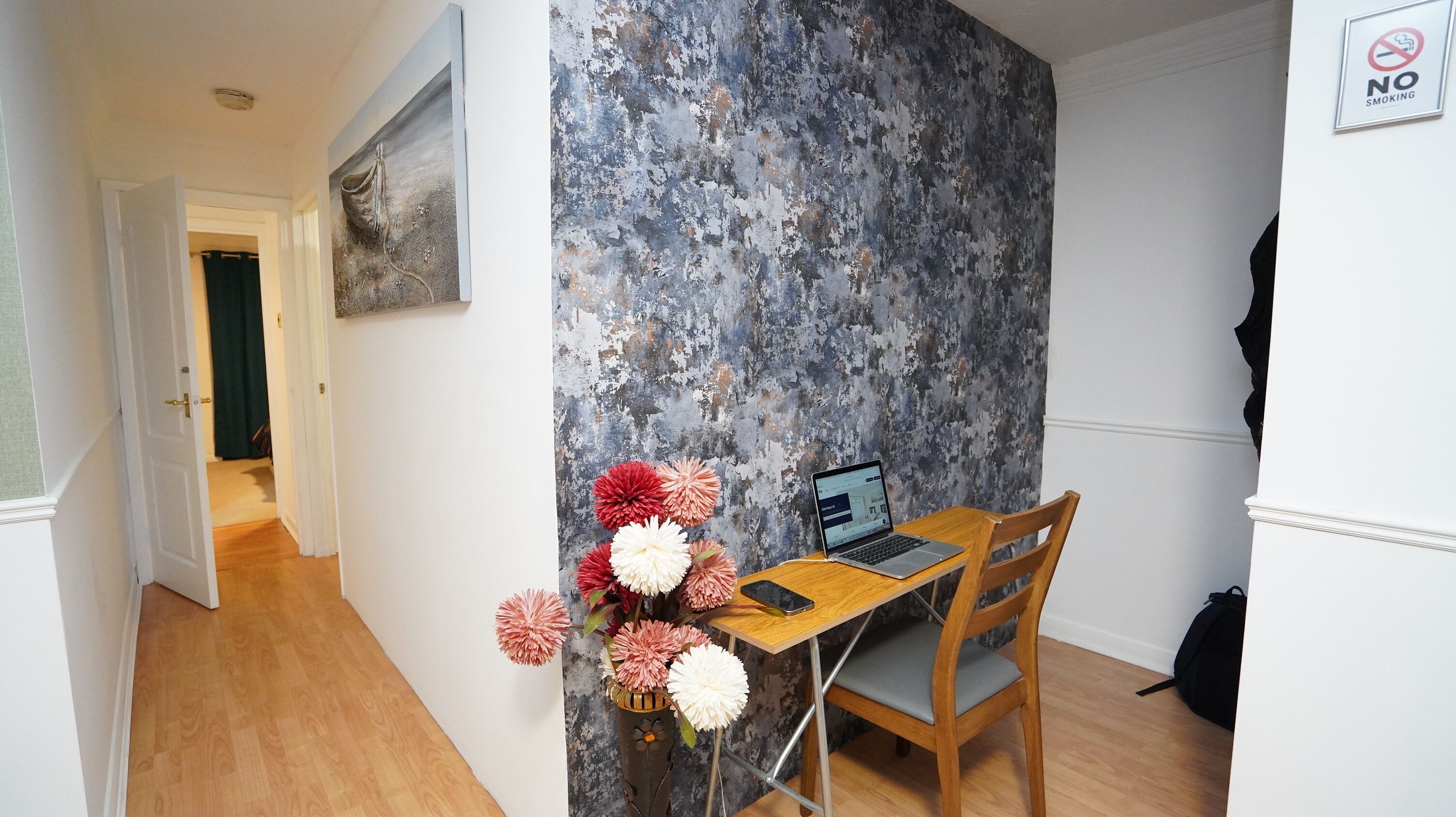 Una habitación con un escritorio de madera, una computadora portátil y un florero con flores.