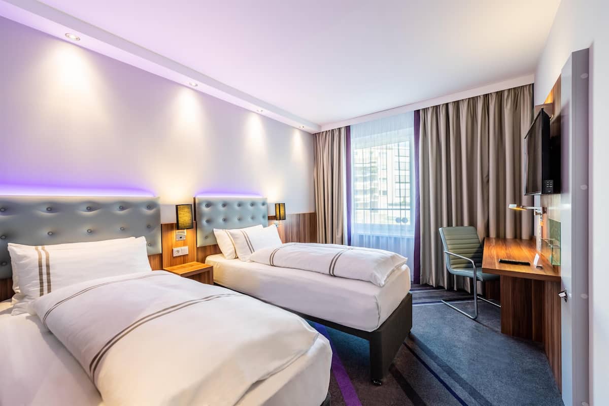 Une chambre d’hôtel avec deux lits, un bureau, une chaise, une télévision et une fenêtre avec des rideaux.