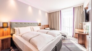 A hotel room with two beds, a desk, a TV, and a large window with curtains.