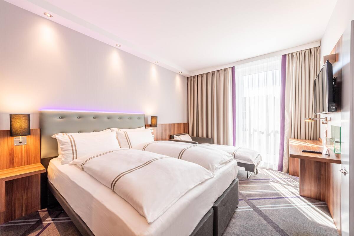 Une chambre d’hôtel avec deux lits, un bureau, une télévision et une grande fenêtre avec des rideaux.