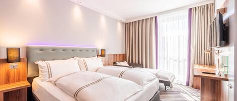 Quarto de hotel com duas camas, uma escrivaninha, uma televisão e uma janela grande com cortinas.