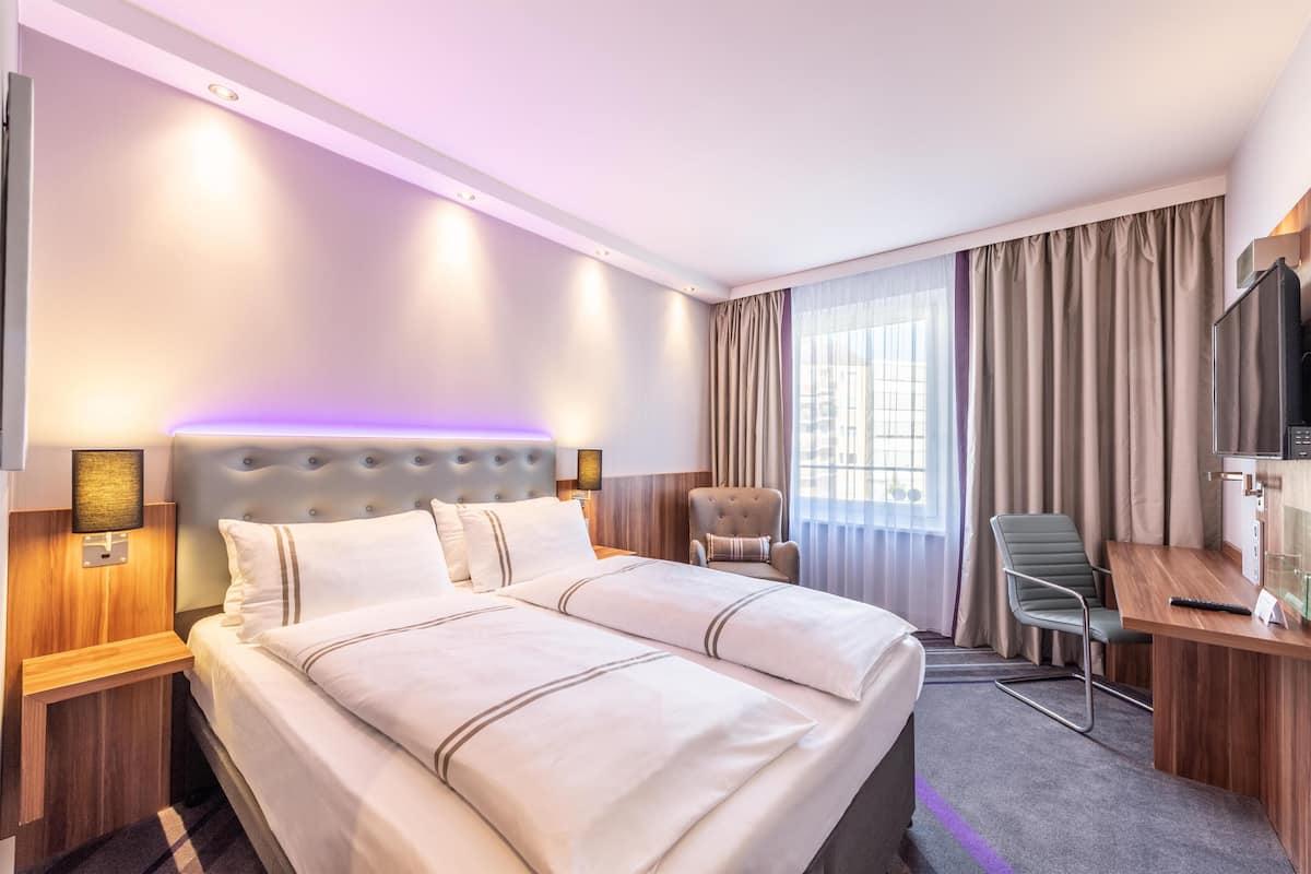 Une chambre d’hôtel avec un grand lit, un bureau, une chaise, une télévision et une fenêtre avec des rideaux.