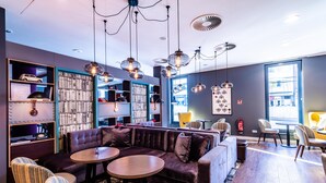 A modern lounge area with a sectional sofa, round tables, striped chairs, a bookshelf, and pendant lighting.